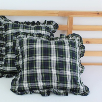 Almofadas xadrez verde escuro com bordas frisadas sobre cama de madeira clara