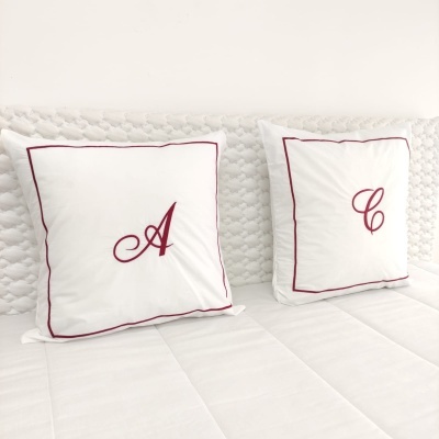 Duas almofadas brancas com letras A e C bordadas em vermelho sobre sofá branco