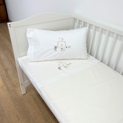 Cama de bebé branca com lençóis brancos bordados com ursinho e girafa