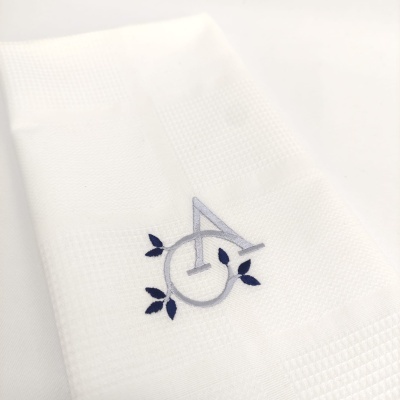 Toalha branca com bordado gris e azul de letras A O com folhas