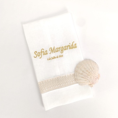 Toalha branca bordada com texto dourado e concha marinha