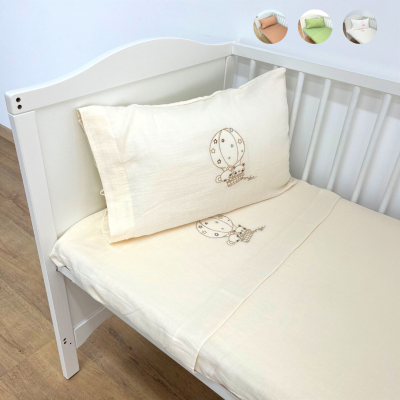 Cama de bebé branca com lençóis creme bordados com balão de ar quente numa sala com chão de madeira clara