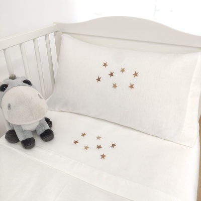 Roupa de cama de berço branca com estrelas douradas e peluche cinza em berço branco