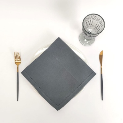 Mesa posta vista de cima com guardanapo cinzento, talheres e copo de vidro.