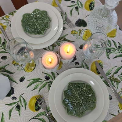 Mesa de jantar com toalha de limões, pratos brancos e pequenos pratos verdes em forma de folha, velas e jarro de vidro