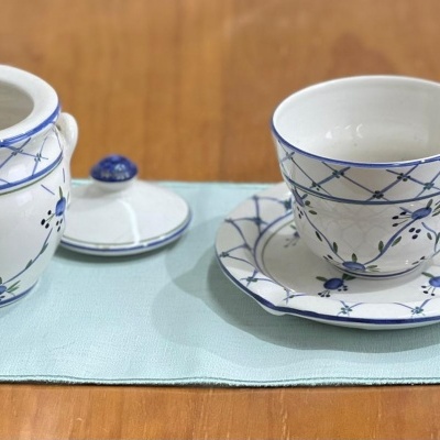 Conjunto de chá porcelana branca com padrão azul sobre pano azul claro e mesa de madeira