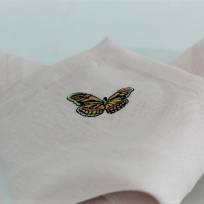 Guardanapo rosa claro com bordado de borboleta sobre prato branco
