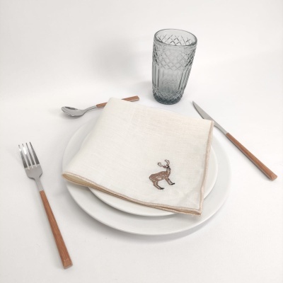 Conjunto de talheres com cabos em madeira, guardanapo branco com bordado de rena, pratos brancos e copo de vidro cinzento