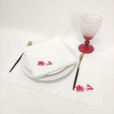 Conjunto de guardanapo e individual brancos com bordados vermelhos, prato branco, talheres e copo vermelho