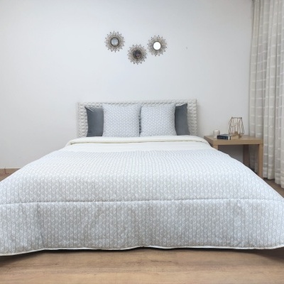 Cama de casal com roupa de cama cinza claro e branco, mesa de cabeceira de madeira clara, cortina bege e parede branca