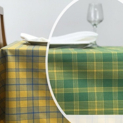 Toalha de mesa xadrez verde e amarela sobre mesa com cadeira de madeira e copo de vidro