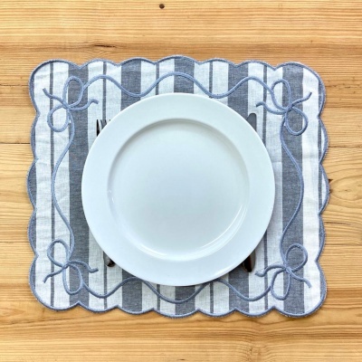 Lugar americano de tecido azul e branco com prato branco e talheres sobre mesa de madeira