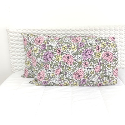 Almofadas florais coloridas sobre cama branca com cabeceira trançada