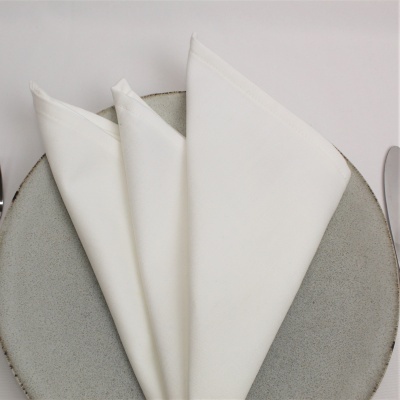 Guardanapo de tecido branco dobrado sobre prato cinza com talheres ao lado