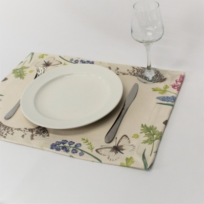 Conjunto de jantar com prato branco, talheres de metal, individual com padrão floral e borboleta e copo de vidro