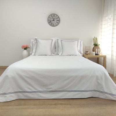 Cama com roupa branca riscada e decoração minimalista num quarto claro