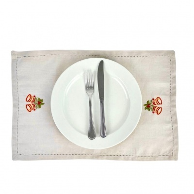 Individual de mesa bege com bordados de sinos natal e talheres sobre prato branco
