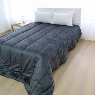 Cama com edredão cinza escuro e almofadas brancas num quarto com chão de madeira