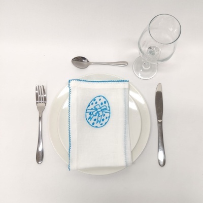Mesa posta com talheres metálicos, prato branco com guardanapo decorativo azul e taça de vidro