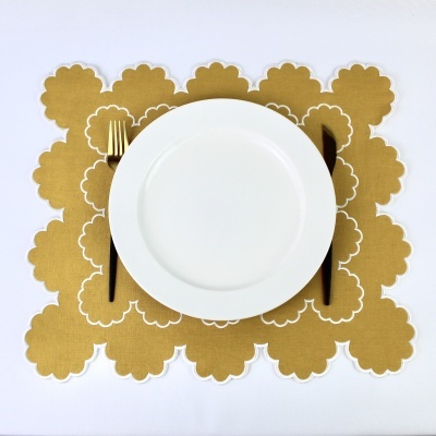 Prato branco com talheres dourados e preto sobre individual amarelo com padrão floral