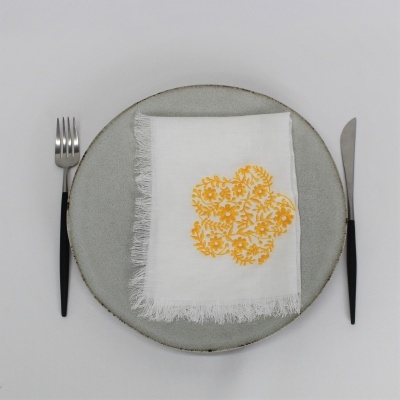 Prato cinzento com guardanapo branco bordado amarelo e talheres pretos