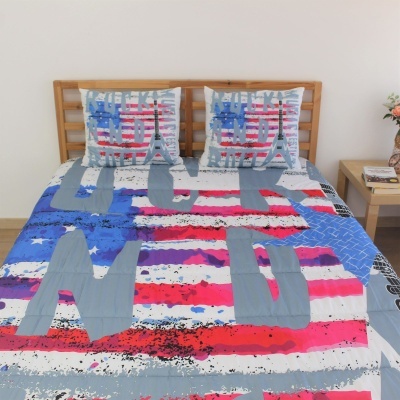 Roupa de cama com padrão de riscas e letras em tons cinza, vermelho, branco e azul, em cama com cabeceira de madeira clara