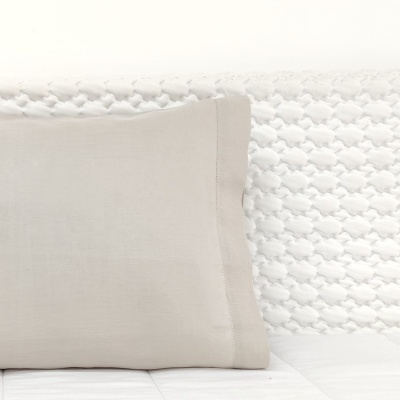 Travesseiro bege claro sobre cama branca com cabeceira texturizada branca.