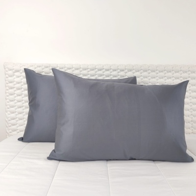 Duas almofadas cinzentas sobre cama branca com cabeceira texturizada