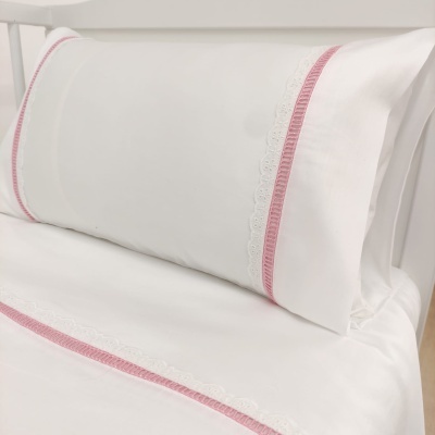 Conjunto de roupa de cama branca com detalhes rosas e renda branca num ambiente de quarto