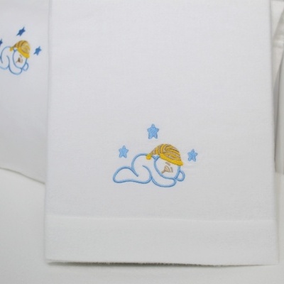 Lençóis brancos com bordado de ursinho azul e chapéu amarelo