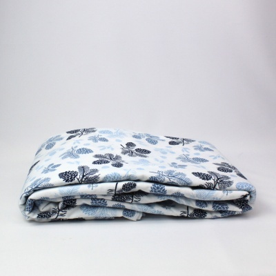 Manta dobrada com padrão de folhas azuis e pretas em fundo branco.