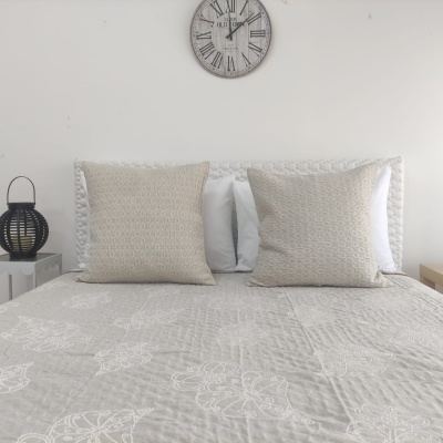 Cama com almofadas cinza, edredão cinza com padrão floral, relógio de parede com números romanos