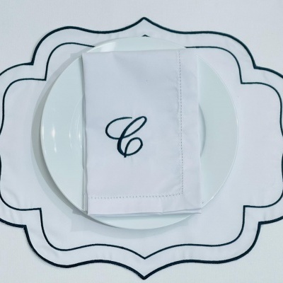 Guardanapo branco com letra C preto sobre prato branco e tapete branco com bordas pretas
