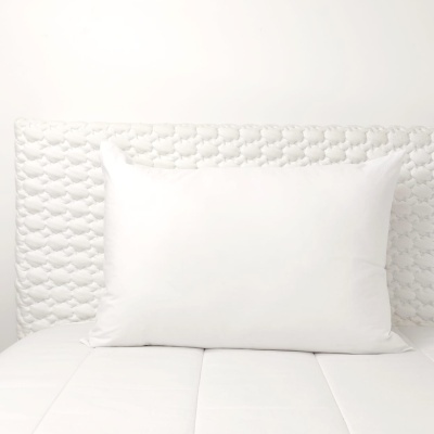 Almofada branca retangular sobre cama com colchão branco e cabeceira estofada texturizada branca