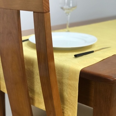 Mesa de madeira com toalha amarela, prato branco, garfo e copo de vidro