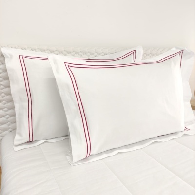 Duas almofadas brancas com linhas vermelhas na borda sobre cama branca