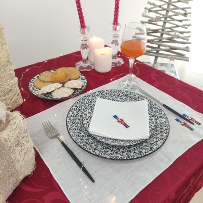 Conjunto de jantar elegante com pratos padrão preto e branco, talheres e decoração natalícia sobre mesa vermelha