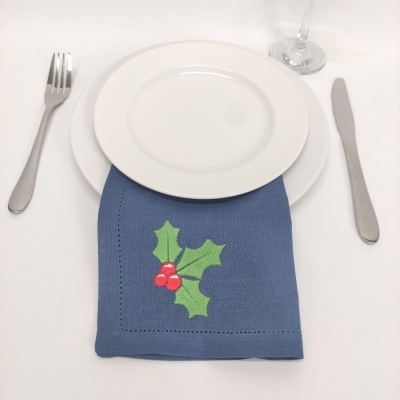 Pratos brancos sobre um guardanapo azul com estampa de azevinho em disposição de mesa com talheres e copo