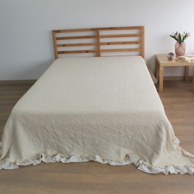 Cama com colcha bege e cabeceira de madeira junto a mesa de cabeceira em ambiente claro