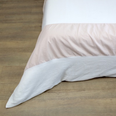 Lençol para cama em duas cores bege rosado e cinzento claro sobre chão de madeira clara