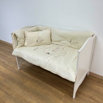 Sofá branco de madeira com almofadas creme bordadas com ursos e texto 'HUG'