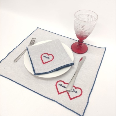 Conjunto de mesa com guardanapo e individual de tecido, prato branco, talheres metálicos e copo vermelho