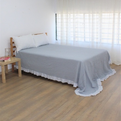Quarto com cama de madeira clara e colcha cinzenta com aba branca, almofadas brancas e mesa de cabeceira com livro