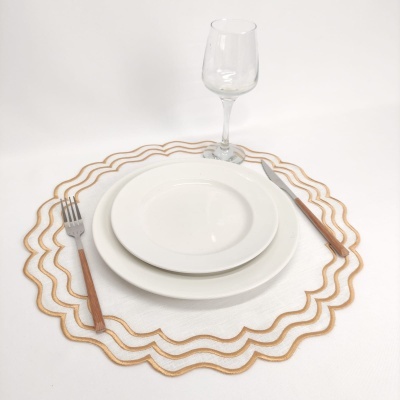 Conjunto de jantar com pratos brancos, talheres de cabo de madeira, taça de vidro e jogo americano branco com bordas douradas onduladas.