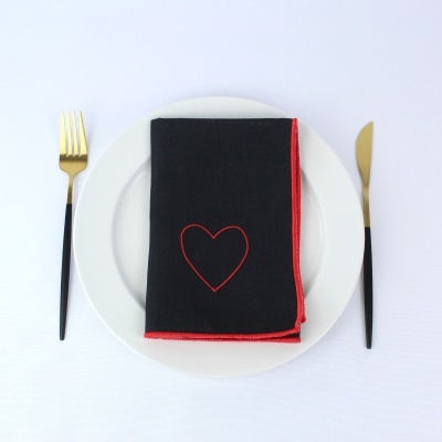 Conjunto de talheres dourados com guardanapo preto com bordas vermelhas e coração bordado, em prato branco