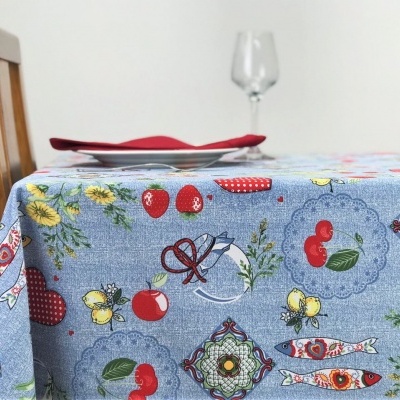 Toalha de mesa azul com padrão colorido de frutas, flores e peixes numa mesa com prato e copo