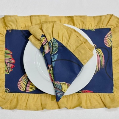 Conjunto de guardanapo, sousplat e toalha azul com folhas coloridas e borda amarela, prato branco ao centro
