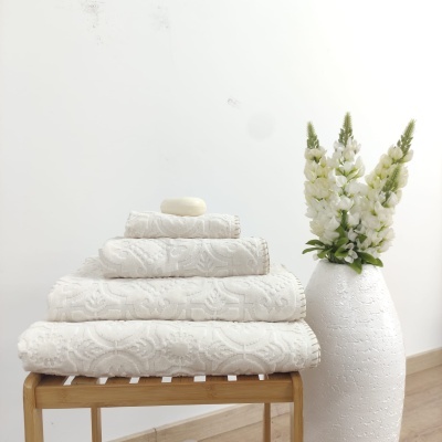 Toalhas brancas texturizadas empilhadas no banco de madeira com sabão e vaso branco com flores ao lado