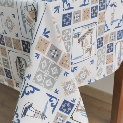 Toalha de mesa estampada com padrão de azulejos em azul, bege e branco sobre mesa de madeira clara