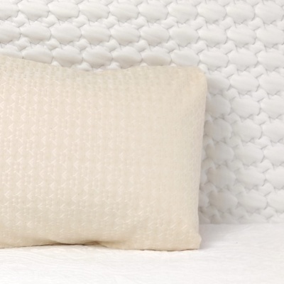 Travesseiro creme com padrão geométrico em cama com fundo de nuvens brancas em relevo